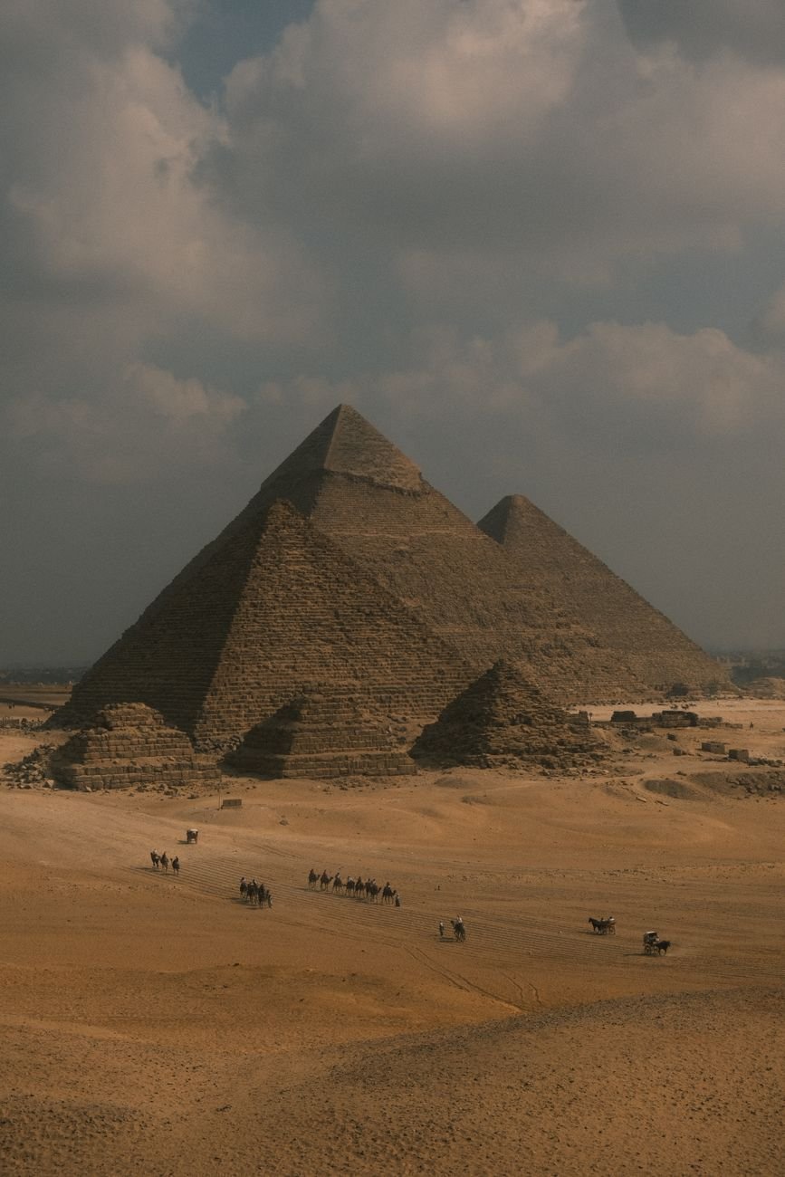 Scenic view of the Pyramids of Giza at dusk, with camels traversing the desert landscape.